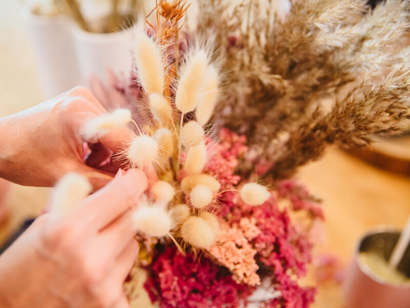 Two hands adjusting flowers in a dried display